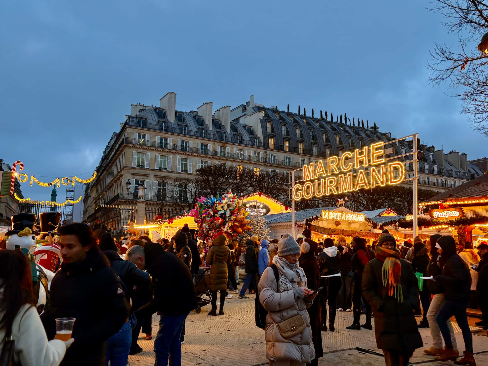 Paris Christmas market at Tuileries Gardens in the evening. Decorations lit up and Haussmann buildings in background.