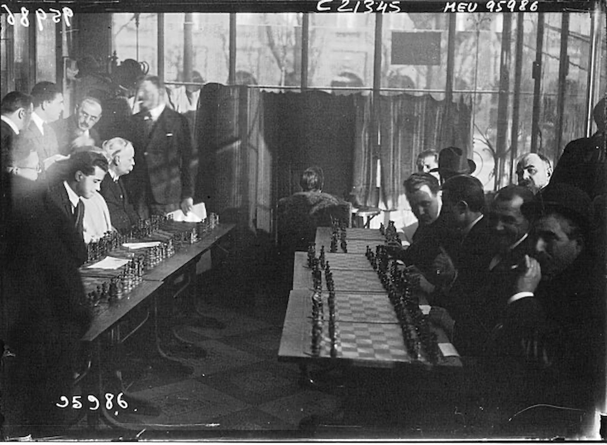 Black and white photo of people sitting around chess tables in an old French café