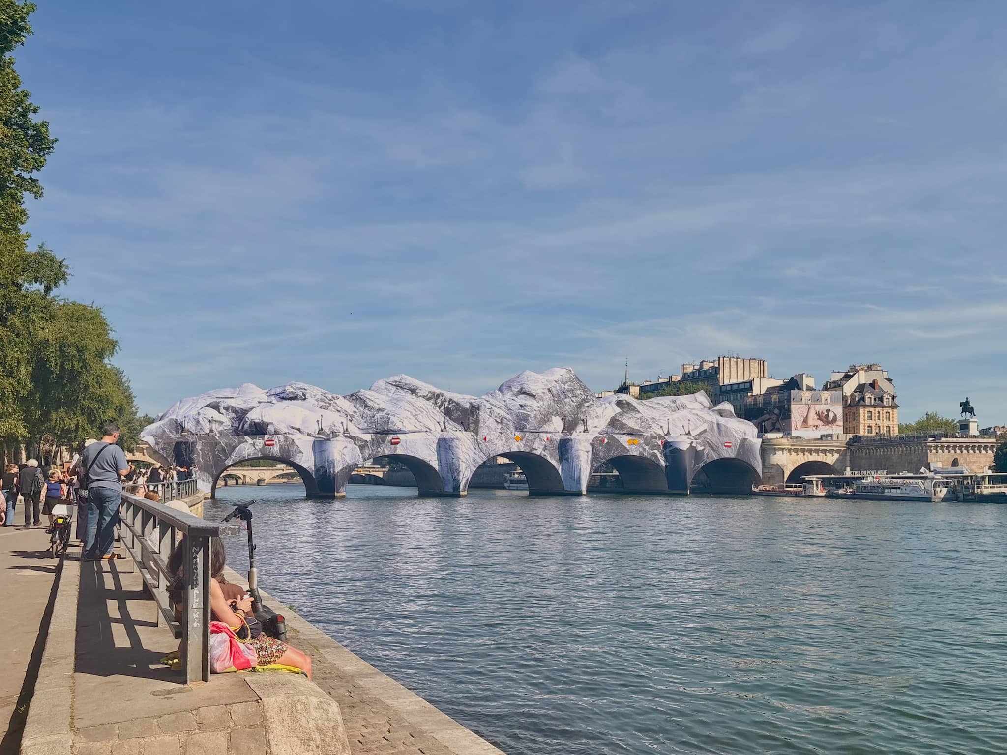 Pont Neuf with the Caverne installation, blue sky and sunny day, people sitting by the Seine