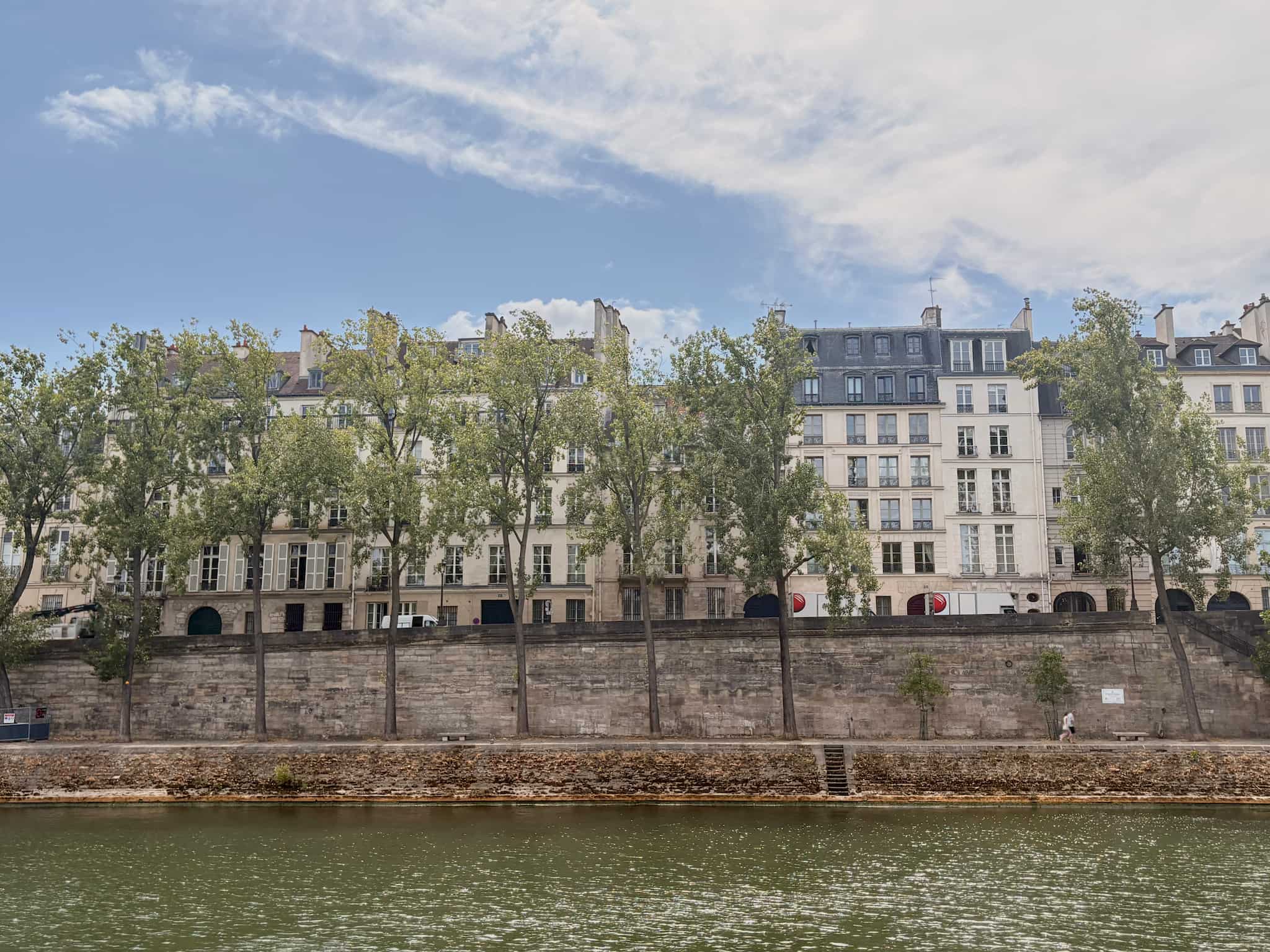 Parisian Haussmann buildings on a quai by the Seine, tall trees in front.