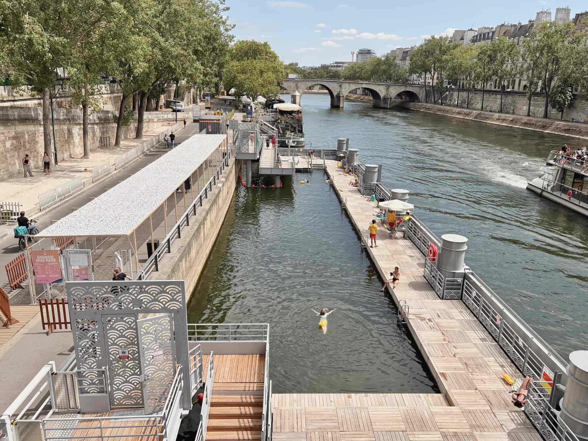 Seine swimming site view from bridge, girl swimming and others sitting by the water.