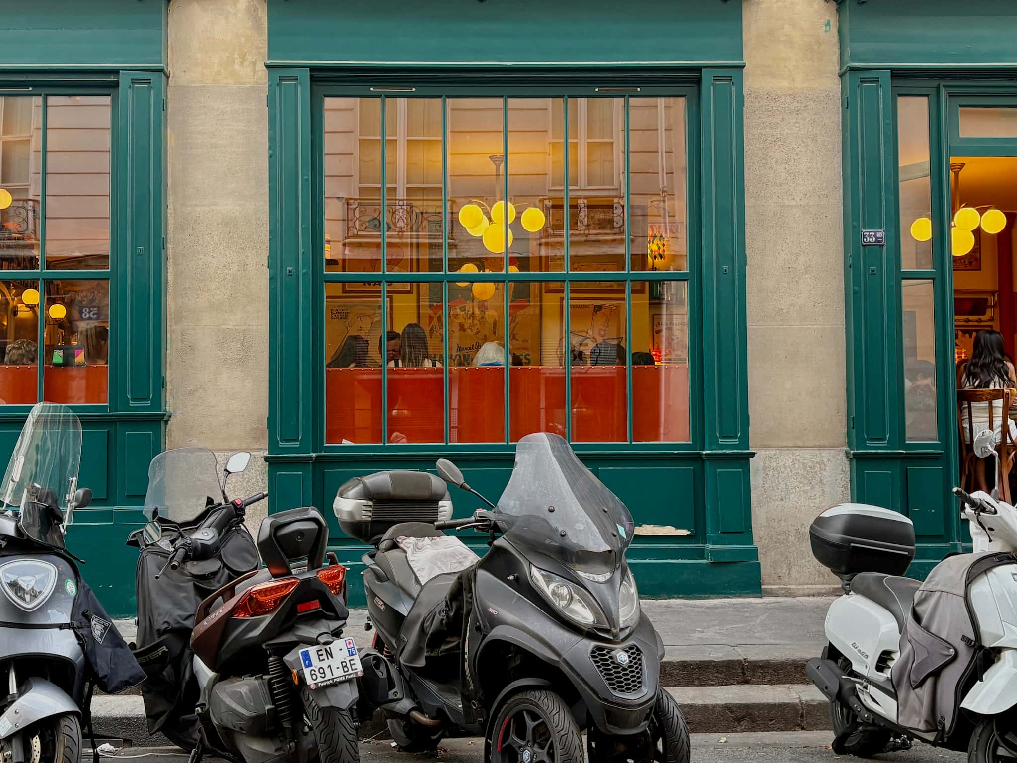 Green windows of Parisian restaurant Chez Janou, people eating inside and scooters parked in front of the windows