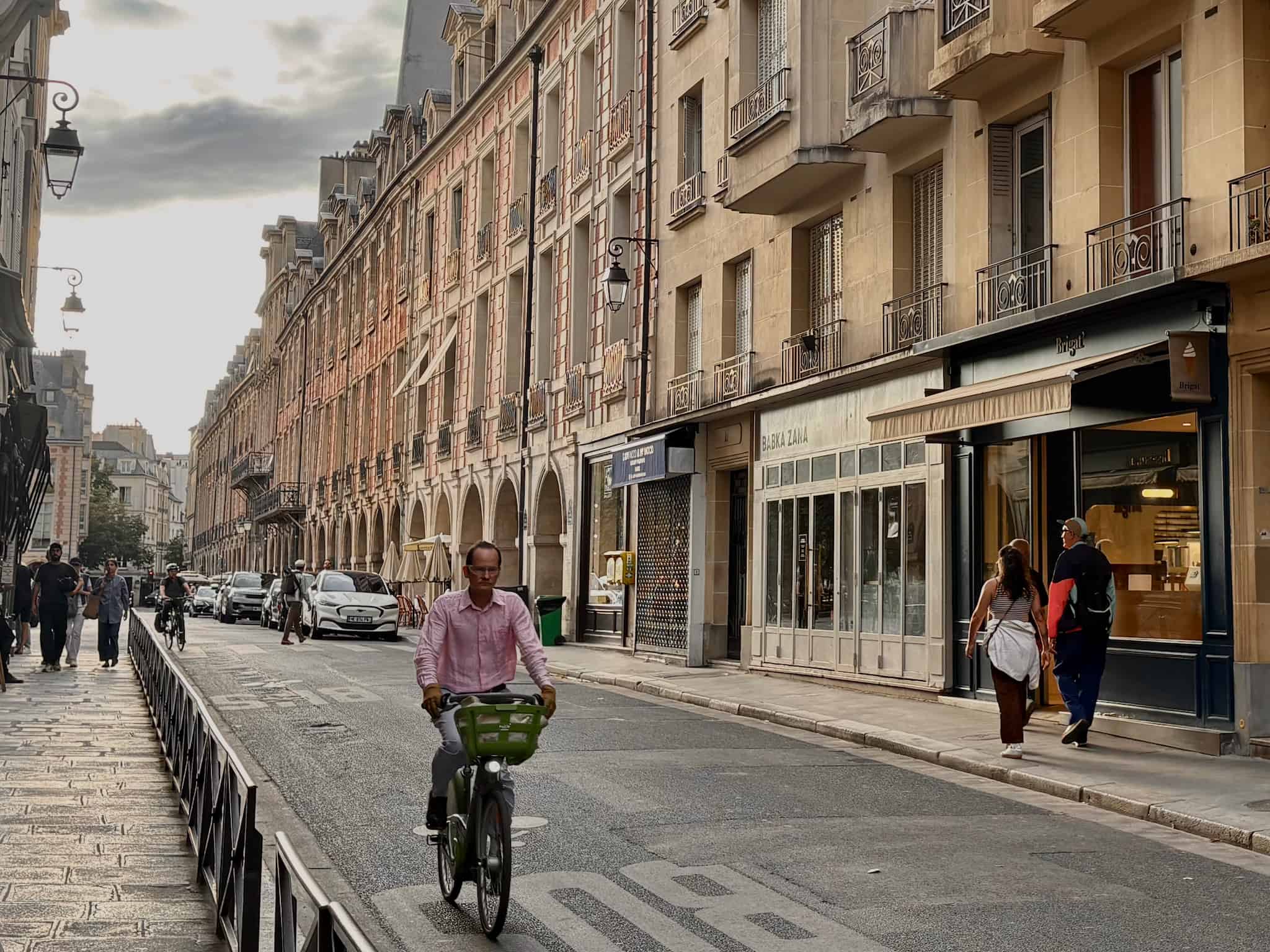 A man on a bike rides by Parisian red brick buildings by Place des Vosges